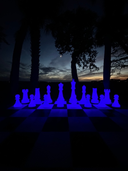 Bright blue landscape lighting illuminates massive oversized chess set at the edge of a salt marsh on Hilton Head Island at night