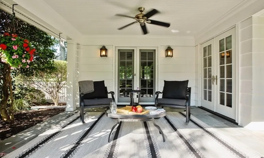 Cozy outdoor seating area with warm antique carriage lights and dark overhead ceiling fan with natural sunlight flooding in.