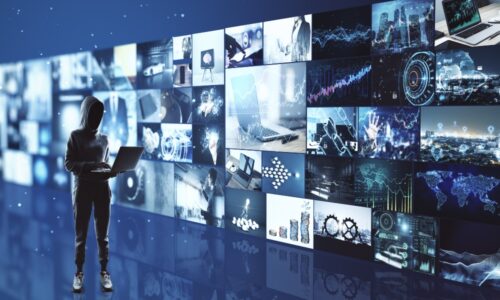 Spying concept with hacker working on laptop and media wall with video shots on background to represent Vo1d botnet hack threat